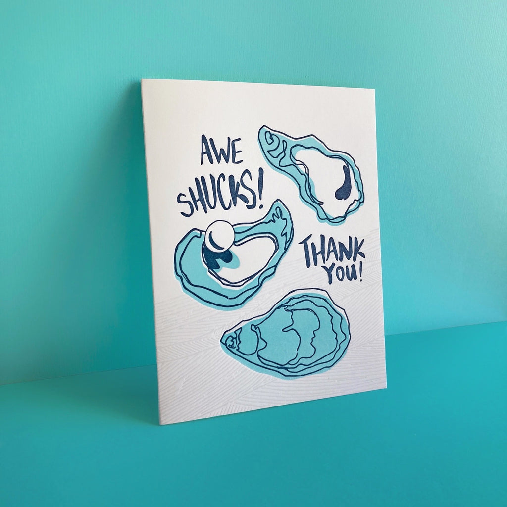 Letterpress thank you card with three oysters - words "Awe Shucks! Thank you!". Shown on an aqua background.