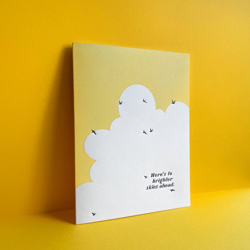 birds flying in sky with words "here's to brighter skies ahead" card featured on a yellow background 