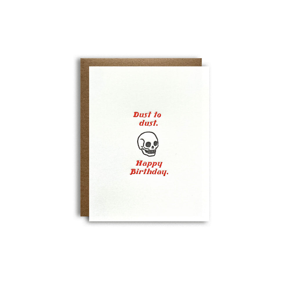 Skull with red lettering "dust to dust, happy birthday" funny letterpress birthday card shown on a white background with a kraft paper envelope