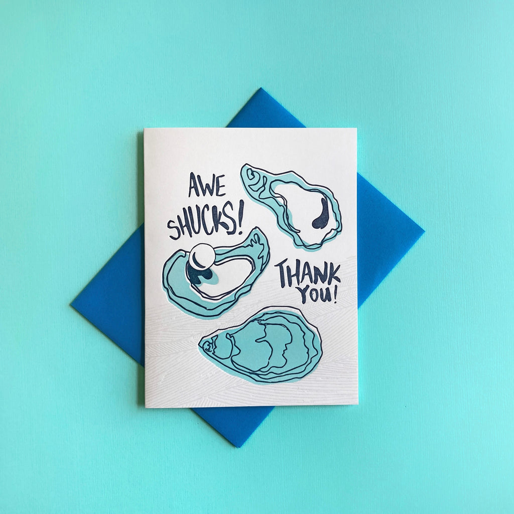 Letterpress thank you card with three oysters - words "Awe Shucks! Thank you!". Shown with a blue envelope on an aqua background