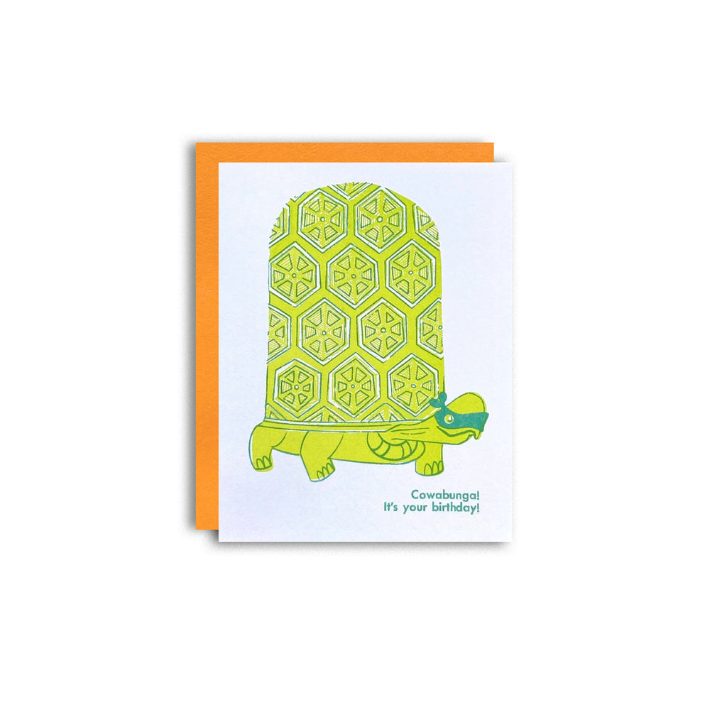 Turtle wearing TMNT style ninja face mask with the phrase "Cowabunga! It's your birthday" risograph greeting card. Shown with a neon orange envelope on a white background