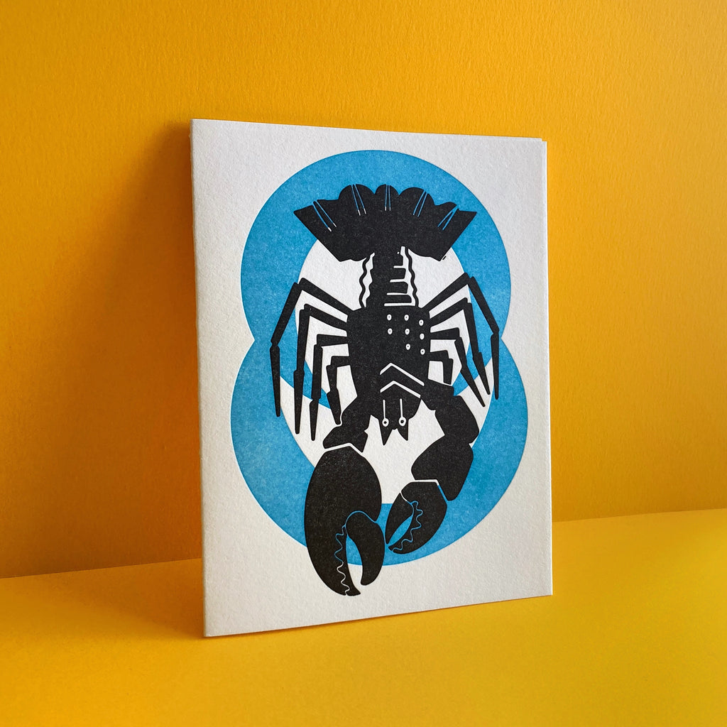  Cancer zodiac letterpress birthday card. Lobster Crawdad Crayfish black letterpress printed. Neon blue pattern in background symbolizing water element. Shown on mustard yellow background.